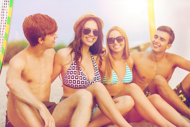 Amitié, mer, vacances d'été, sports nautiques et concept de personnes - groupe d'amis souriants portant des maillots de bain et des lunettes de soleil avec des planches de surf sur la plage