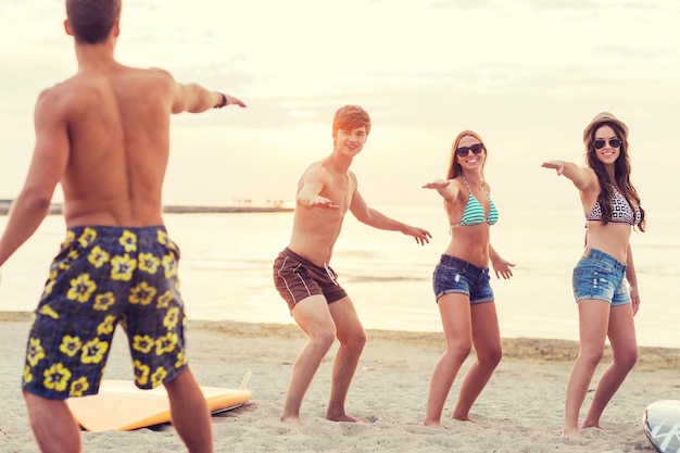 Amitié, mer, vacances d'été, sports nautiques et concept de personnes - groupe d'amis souriants portant des maillots de bain et des lunettes de soleil avec des planches de surf sur la plage