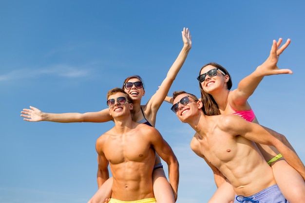 Amitié, mer, vacances d'été, vacances et concept de personnes - groupe d'amis souriants portant des maillots de bain et des lunettes de soleil s'amusant sur la plage