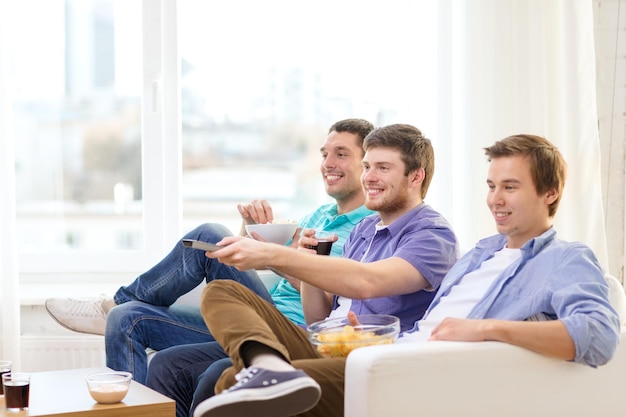 Amitié, technologie et concept de maison - amis masculins souriants avec télécommande et malbouffe à la maison