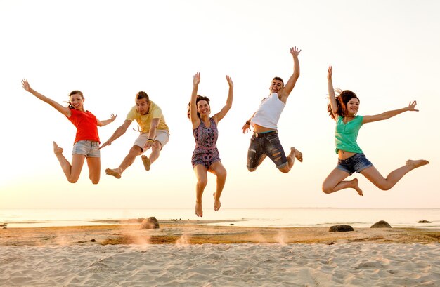 Amitié, vacances d'été, vacances, fête et concept de personnes - groupe d'amis souriants dansant et sautant sur la plage