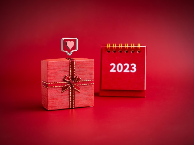 Amour 3d comme des icônes de coeur flottant sur une petite boîte cadeau rouge avec calendrier de bureau 2023 sur fond rouge Cadeau spécial pour l'anniversaire et les anniversaires de la Saint-Valentin