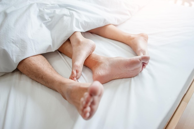 Amour couché dans son lit à l'hôtel embrassant sur des draps blancs gros plan jambes