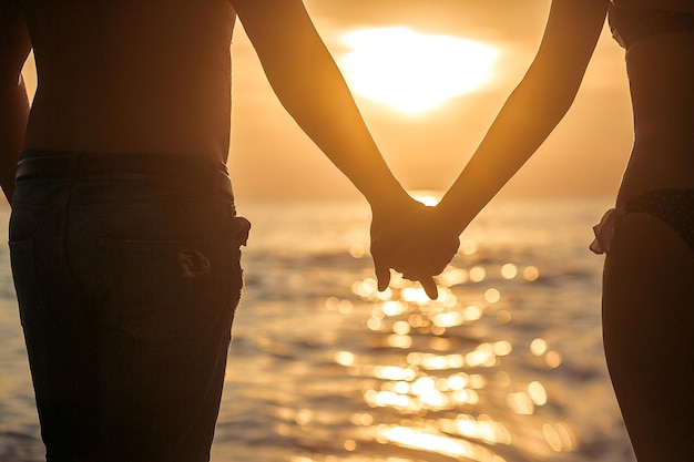 Amour - couple romantique main dans la main, coucher de soleil sur la plage. Amoureux ou jeune couple marié en romance sur un magnifique coucher de soleil sur la plage. Jeune femme et homme amoureux marchant main dans la main sur la plage.
