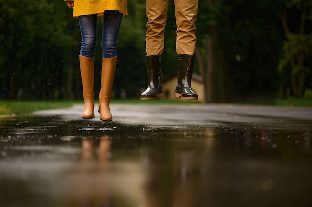 Amour couple saute dans une flaque d'eau dans le parc, jour de pluie d'été. Homme et femme sous parapluie sous la pluie, rendez-vous romantique sur chemin de marche, temps humide dans la ruelle