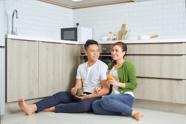 L'amour est dans l'air. Beau jeune couple de boire du café et du jus d'orange assis sur le sol de la cuisine à la maison