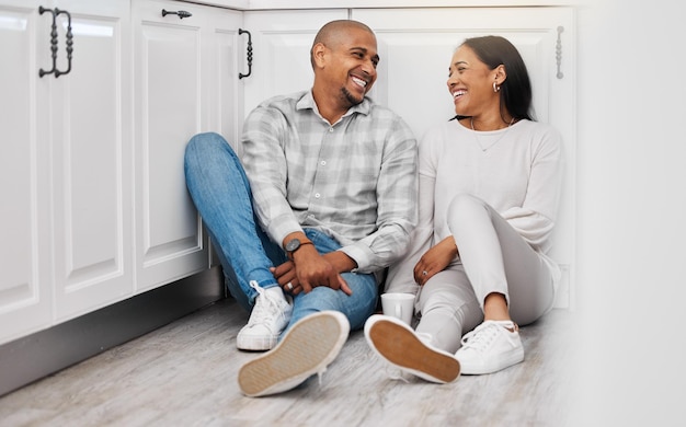 Photo amour heureux et couple se détendre sur un sol parler et se lier dans leur cuisine à la maison avec du café thé de mariage et homme assis avec une femme riant et appréciant la conversation et la relation à l'intérieur