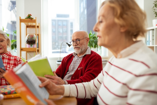 Amour à lire. Agréable homme d'âge tenant un livre vert en le lisant avec des amis