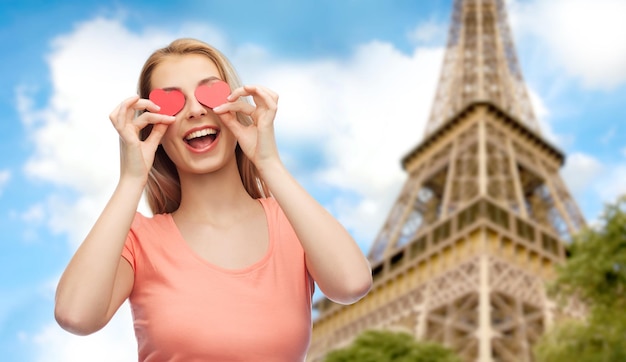 amour, romance, saint valentin et concept de personnes - jeune femme souriante ou adolescente avec des formes de coeur rouge sur les yeux sur fond de tour eiffel de paris