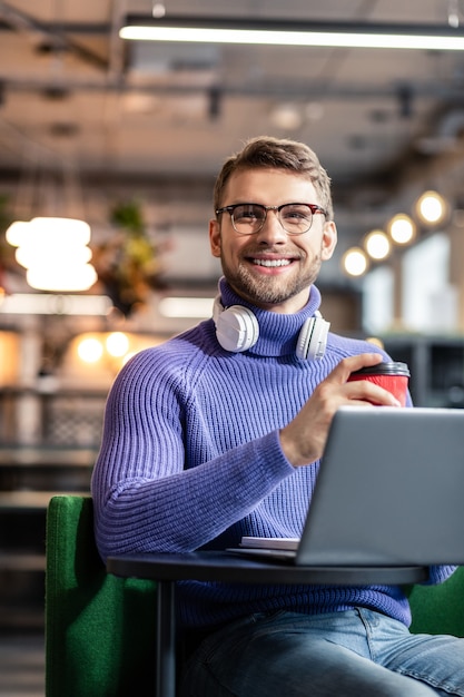 En amour avec le travail. Beau mâle brune exprimant la positivité alors qu'il était assis en face de son ordinateur