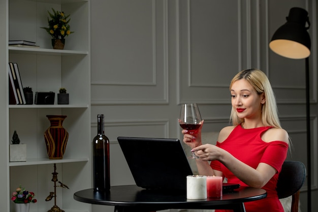 Amour virtuel fille blonde en robe rouge sur date à distance avec du vin pointant vers l'écran