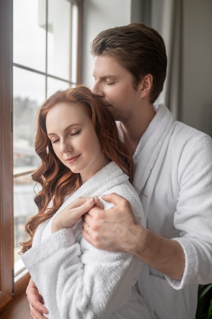 Amoureux. Un homme et une femme en peignoirs blancs se tenant près de la fenêtre et se sentant amoureux