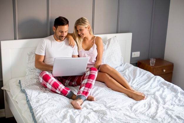 Amoureux intimes utilisant un ordinateur portable assis sur le lit dans la chambre