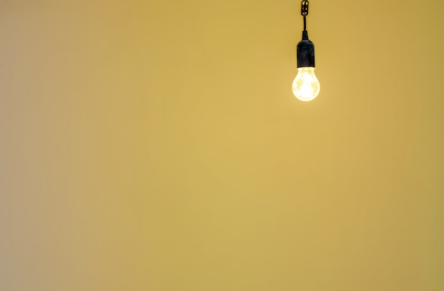 Une ampoule allumée sur le fond d'un mur jaune