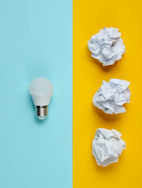 Ampoule à économie d'énergie et boules de papier froissé sur table bleu jaune. Concept d'entreprise minimaliste, idée. Vue de dessus