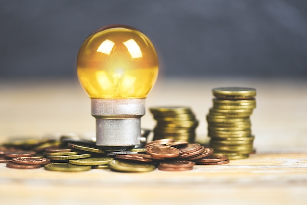 Photo ampoule avec la lumière de la lampe sur des pièces empilées sur une table en bois. idée d'économie d'énergie, économie d'énergie et le concept du monde