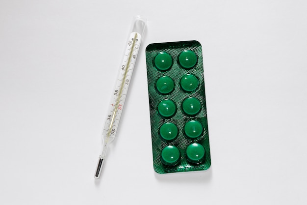 Ampoule verte avec des pilules et un thermomètre sur une surface blanche