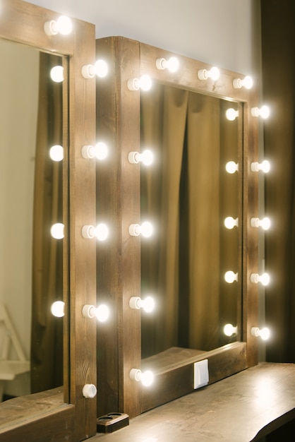 Les ampoules lumineuses sont disposées en ligne verticalement sur la surface du miroir, près de la table de maquillage. Éclairage d'un miroir dans une salle de bain, copyspace