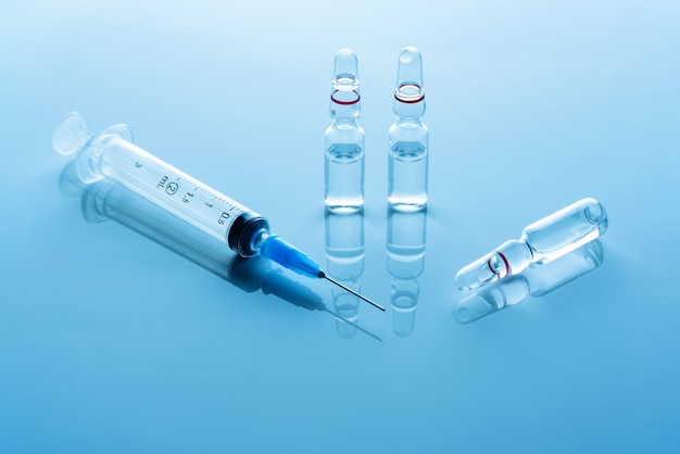 Ampoules avec un vaccin et une seringue médicale sur une surface bleue