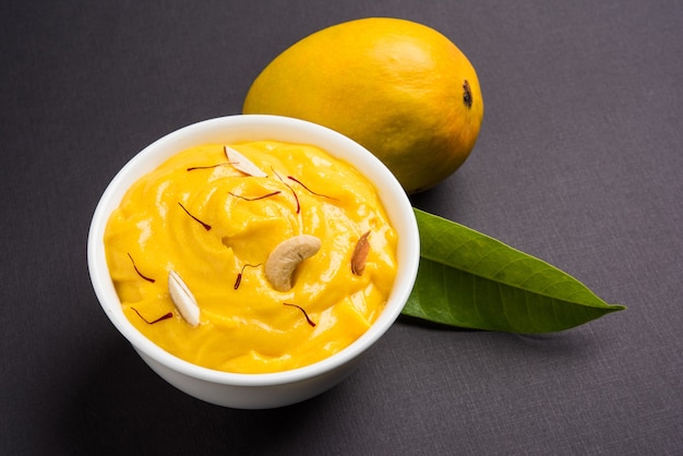 Amrakhand est un yogourt ou Shrikhand aromatisé Alphonso, un bonbon indien populaire servi avec des fruits secs et du safran avec des mangues entières, sur fond coloré. mise au point sélective