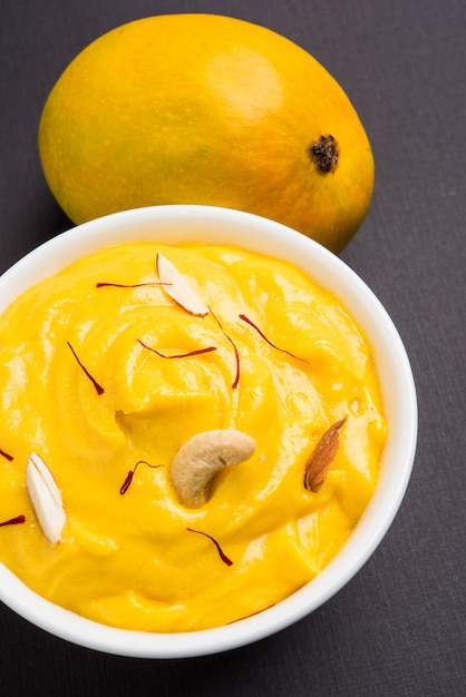 Amrakhand est un yogourt ou Shrikhand aromatisé Alphonso, un bonbon indien populaire servi avec des fruits secs et du safran avec des mangues entières, sur fond coloré. mise au point sélective