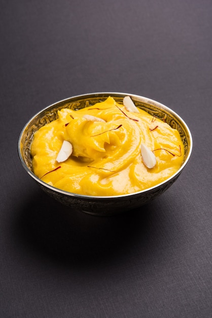 Amrakhand est un yogourt ou Shrikhand aromatisé Alphonso, un bonbon indien populaire servi avec des fruits secs et du safran avec des mangues entières, sur fond coloré. mise au point sélective