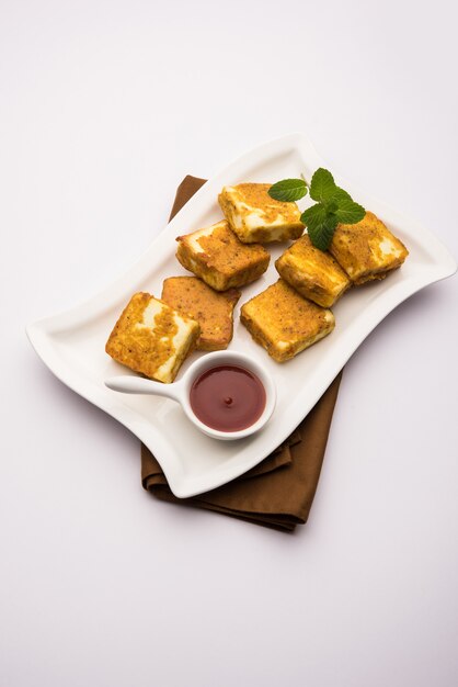 Amritsari Paneer Tikka à base de cubes de fromage cottage trempés dans une pâte à base de besan, de chat masala et d'épices et frits peu profonds dans une poêle, servis avec du ketchup