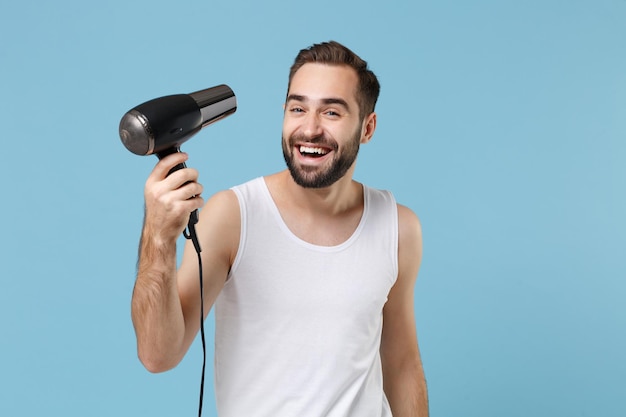 Amusant barbu jeune homme de 20 ans en chemise blanche tenir les cheveux secs isolés sur fond de mur bleu pastel, portrait en studio. Concept de procédures cosmétiques de soins de la peau. Maquette de l'espace de copie.