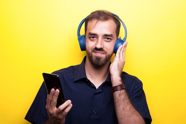 Amusant bon jeune homme appréciant la musique de son smartphone sur fond jaune