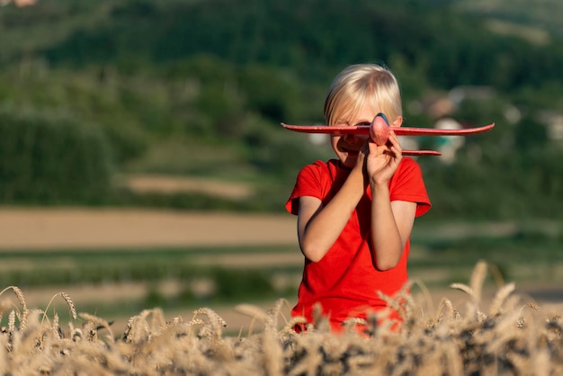 Amusant garçon de 7 ans aux cheveux blonds jouant avec un avion rouge et debout dans des épis de blé mûr Voyage en avion avec des enfants