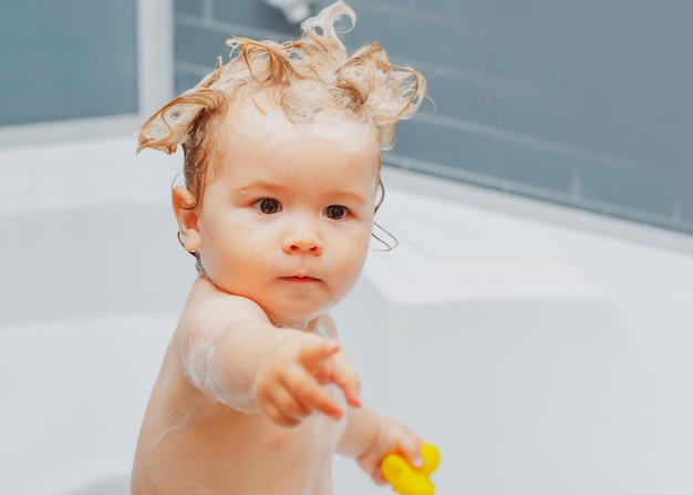 Amusant garçon blond s'amusant avec de l'eau en prenant un bain dans la baignoire baignant bébé enfant heureux avec du savon