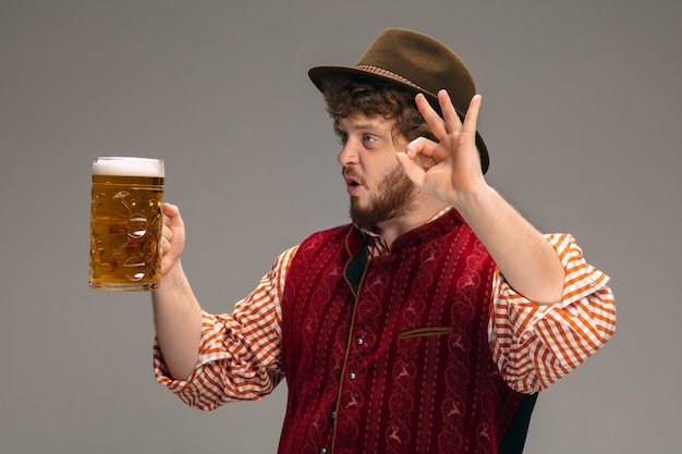 Amusant. Heureux homme vêtu d'un costume traditionnel autrichien ou bavarois faisant des gestes avec une chope de bière sur fond gris studio. Espace de copie. La célébration, l'oktoberfest, le festival, le concept de traditions.