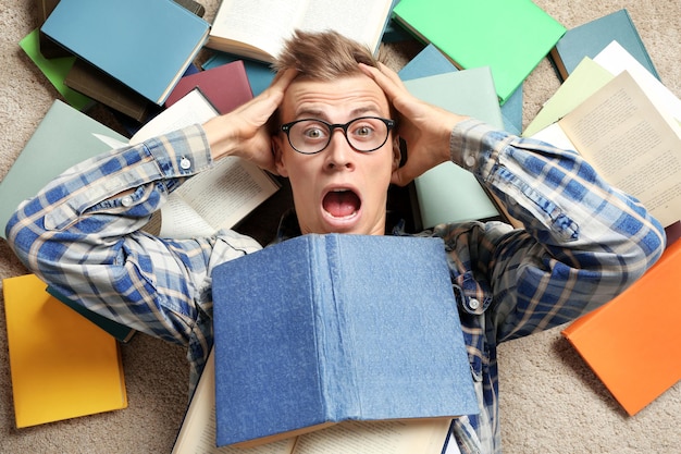 Photo amusant jeune homme allongé sur le sol parmi les livres