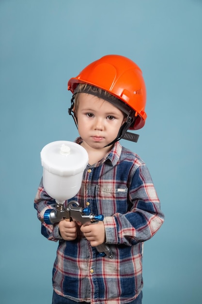 Amusant petit garçon caucasien portant un casque tenant un pistolet électrique, un concept de peintre ou de décorateur.