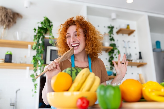 Amusante belle femme chantant dans la cuisine à la spatule dans une cuisine moderne tenant la spatule comme microphone dansant en écoutant de la musique fille ludique s'amusant avec des ustensiles de cuisine préparant la nourriture