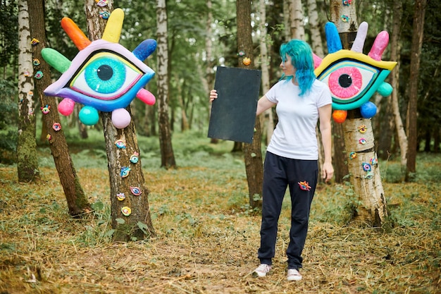 Amusante jeune femme adulte aux cheveux turquoise teints en T-shirt blanc près de l'installation d'art big eye