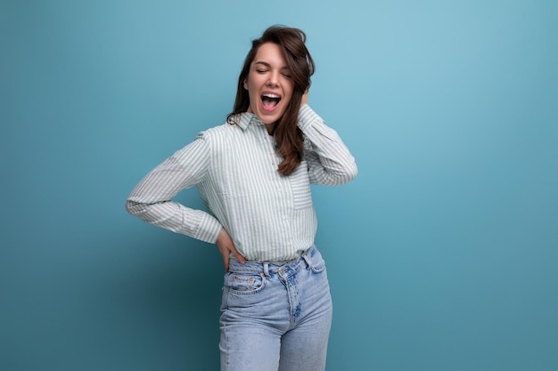 Amusante jeune femme brune vêtue d'une chemise rayée et d'un jean sur fond de studio