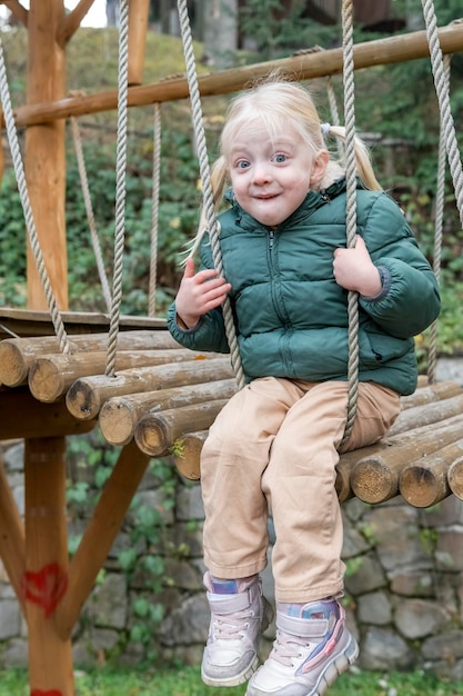 Amusante petite fille joyeuse avec deux queues de cheval assise sur un pont suspendu en bois Cadre vertical