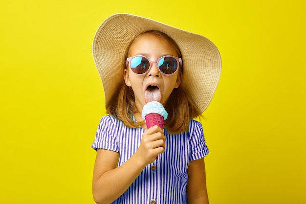 Amusante petite fille en vêtements d'été mangeant de belles glaces debout sur jaune isolé