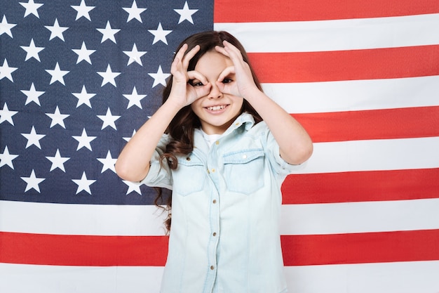 Amusé joyeux ravi fille s'amusant et exprimant la joie en se tenant debout contre le drapeau américain