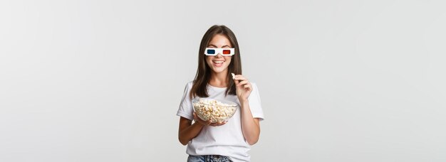 Amusée jolie jeune femme dans des lunettes 3d regardant des films ou des séries télévisées mangeant du pop-corn et souriant ravi