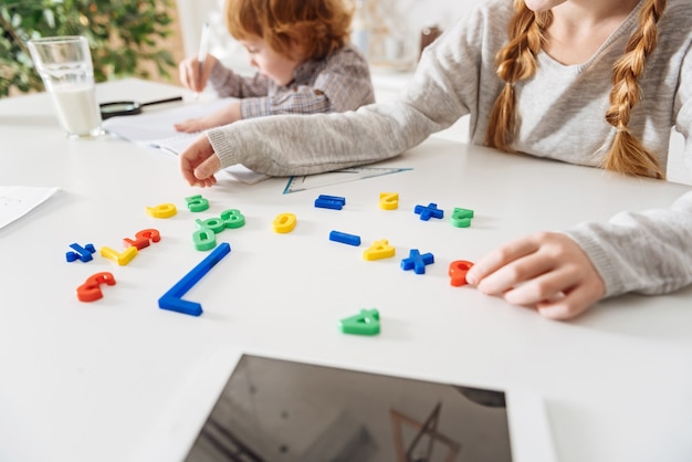 Amusement académique. Dame enthousiaste curieuse intelligente apprendre les mathématiques tout en organisant des nombres en plastique colorés et assis avec son frère à la table