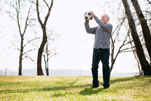 Amusez-vous avec le ballon. Homme d'âge mûr positif exerçant avec ballon et debout sur l'herbe