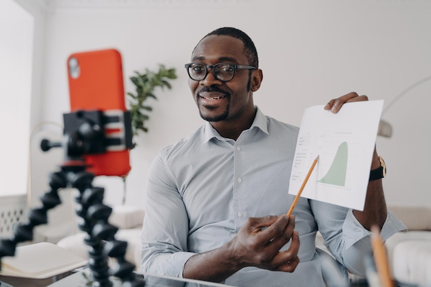 Photo un analyste d'affaires afro-américain montre un graphique économique à ses collègues en ligne par appel vidéo avec téléphone