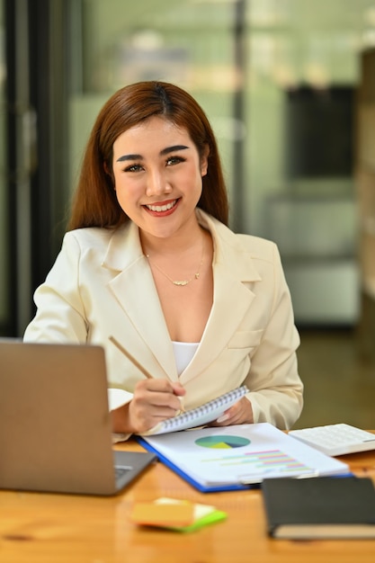 Analyste féminine attrayante vérifiant les résultats de la recherche marketing ou les données statistiques sur un ordinateur portable