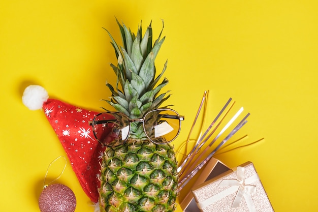 Ananas, bonnet de noel et lunettes de soleil, décor de noël sur fond jaune