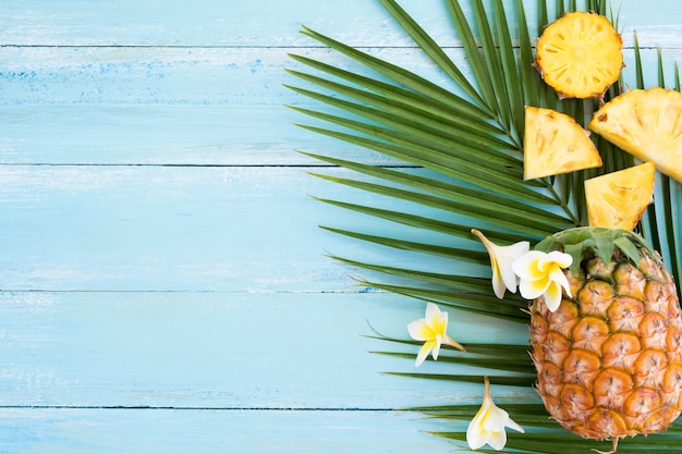 Ananas et branche de palmier sur planche de bois de couleur bleue.