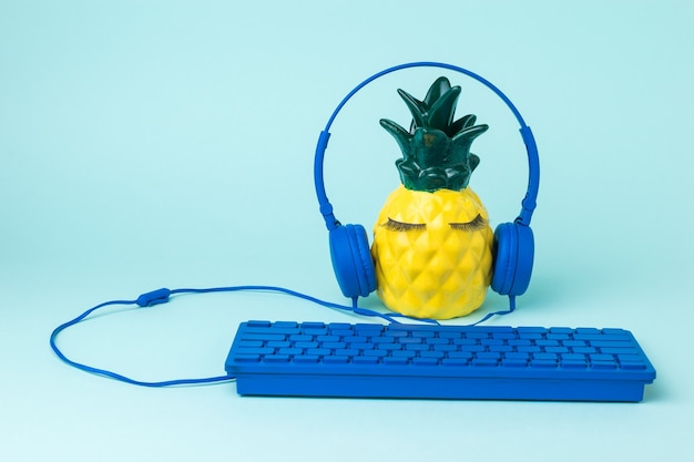 Ananas avec clavier et écouteurs sur une surface bleue. Le concept de la numérisation mondiale.
