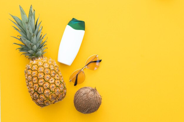 Ananas créatif levant les yeux avec des lunettes de soleil bouteille de crème et cocos isolé sur fond jaune été vacances plage idée modèle de conception copie espace gros plan