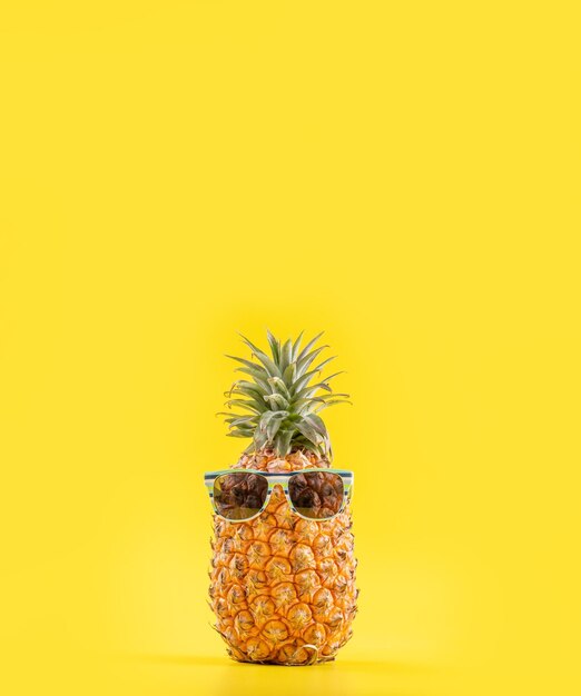 Ananas créatif levant les yeux avec des lunettes de soleil et une coquille isolée sur fond jaune vacances d'été plage idée modèle de conception copie espace gros plan